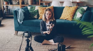 Cheerful girl vlogger is recording video about make-up, cosmetics and tools for her internet videolog using camera. Photo by Vitaly Gariev on Unsplash.
