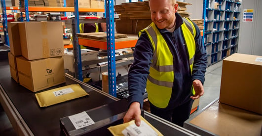 Happy warehouse worker placing parcels on conveyer belt 